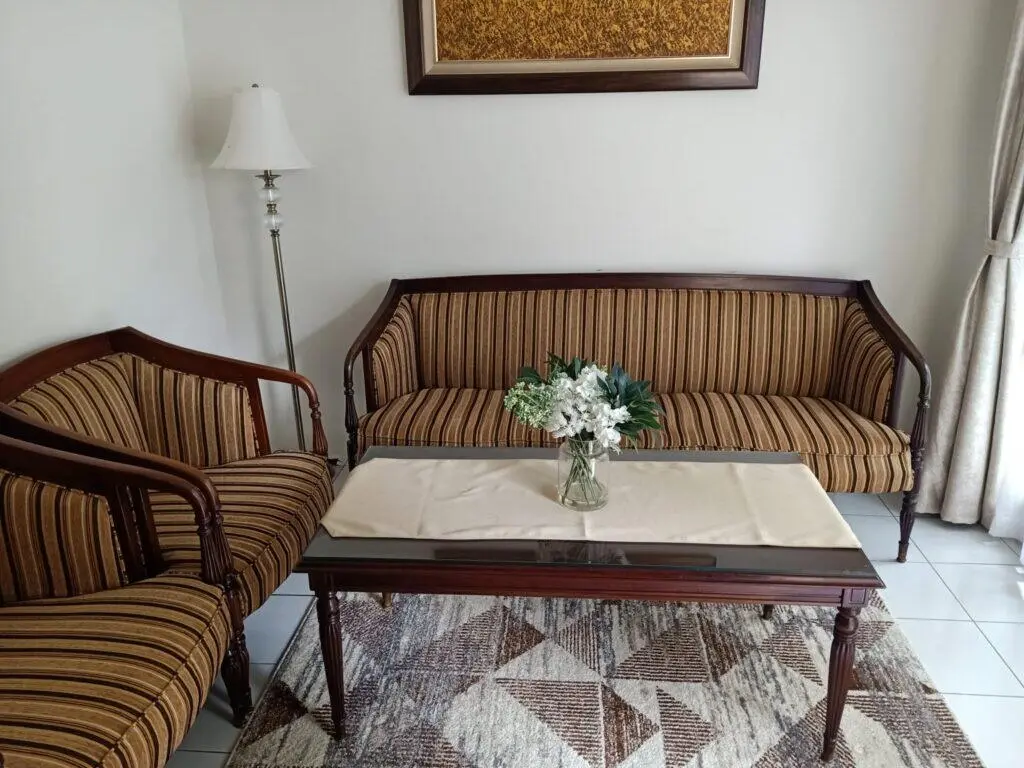 A cozy living room setting featuring two upholstered striped sofas with wooden frames. In the center, there's a glass-top cof