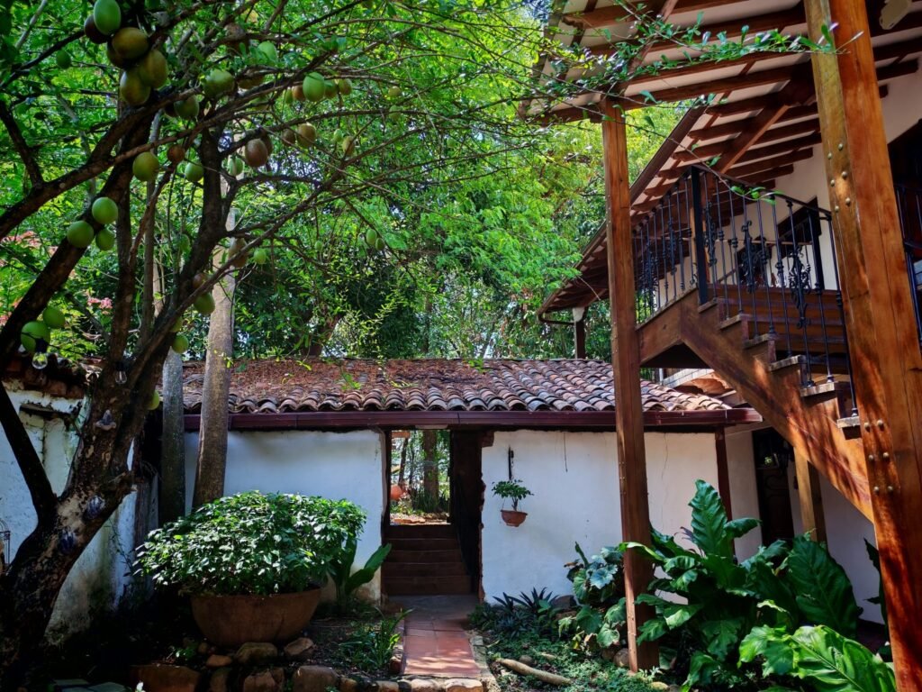A white house with tiled roofs and white walls, the house has an opening in the middle that works as a door, stairs on the si