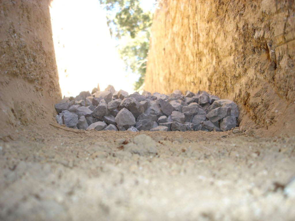 A gravel-lined French drain trench beside a house